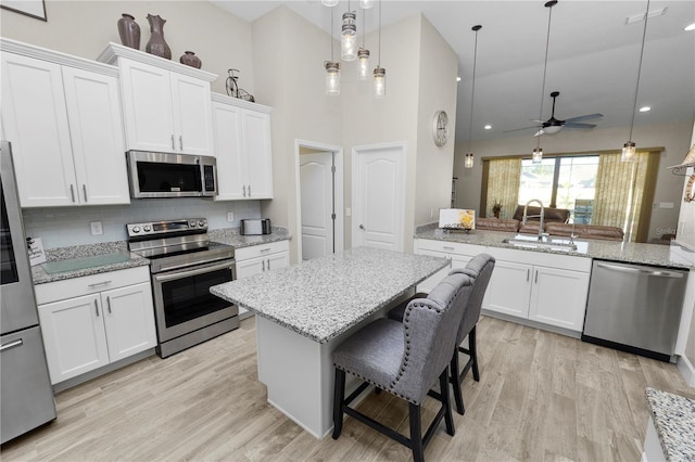 kitchen with a towering ceiling, stainless steel appliances, ceiling fan, sink, and white cabinetry