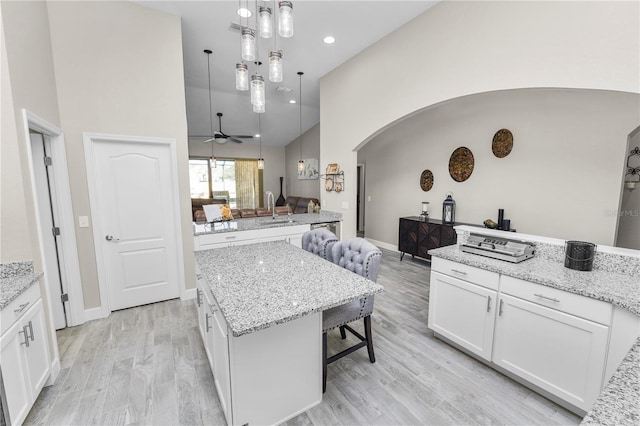 kitchen featuring white cabinetry, a center island, hanging light fixtures, high vaulted ceiling, and light hardwood / wood-style floors