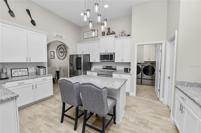 kitchen with washer and clothes dryer, white cabinets, light hardwood / wood-style flooring, light stone countertops, and stainless steel appliances