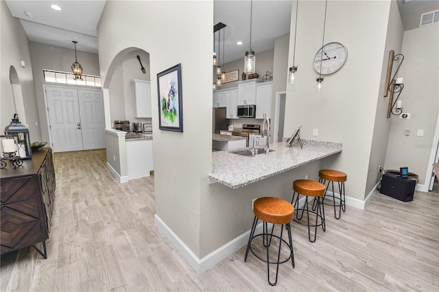 kitchen with pendant lighting, a breakfast bar, white cabinets, kitchen peninsula, and stainless steel appliances