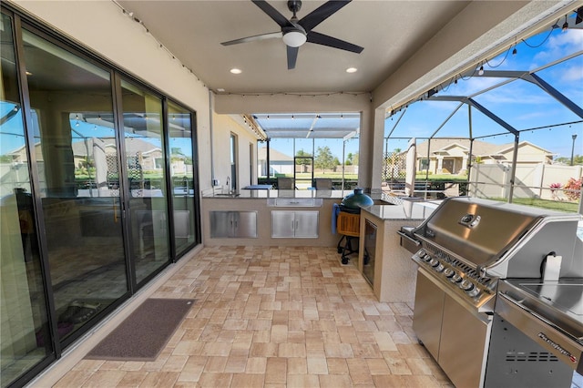 view of patio featuring glass enclosure, ceiling fan, and an outdoor kitchen