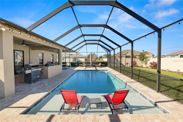 view of pool with an outdoor kitchen, ceiling fan, glass enclosure, a patio area, and a lawn