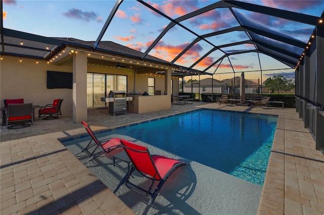 pool at dusk with a patio, glass enclosure, and area for grilling