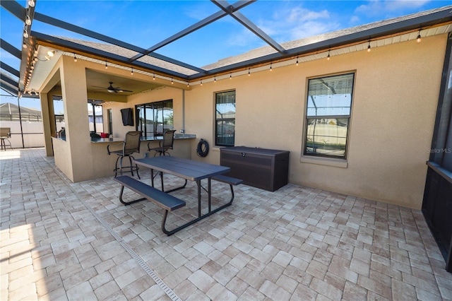 view of patio featuring ceiling fan, exterior bar, and glass enclosure