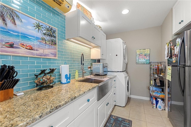 kitchen with backsplash, white cabinets, stainless steel fridge, stacked washing maching and dryer, and light stone counters