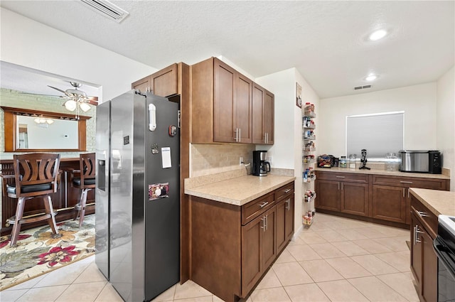 kitchen with ceiling fan, stainless steel fridge with ice dispenser, a textured ceiling, light tile patterned flooring, and range