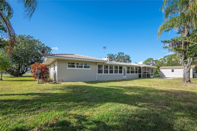 rear view of property featuring a sunroom, a storage unit, and a yard