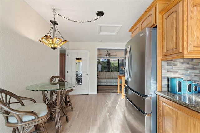 kitchen with decorative backsplash, dark stone countertops, light wood-type flooring, decorative light fixtures, and stainless steel refrigerator