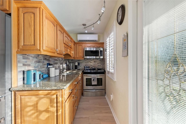 kitchen with a wall mounted air conditioner, light stone countertops, tasteful backsplash, stainless steel appliances, and light hardwood / wood-style floors