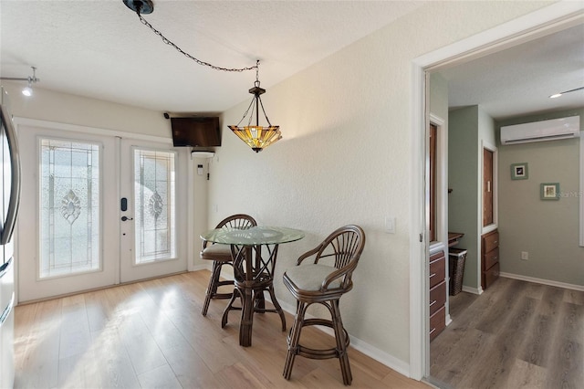 dining room with a wall unit AC, french doors, wood-type flooring, and a textured ceiling