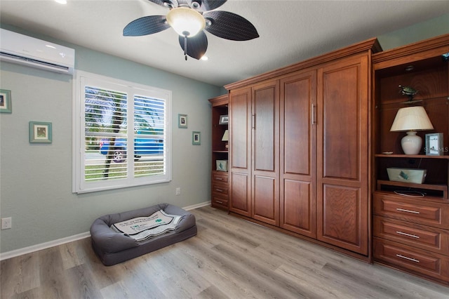 living area featuring a wall mounted air conditioner, light hardwood / wood-style floors, and ceiling fan