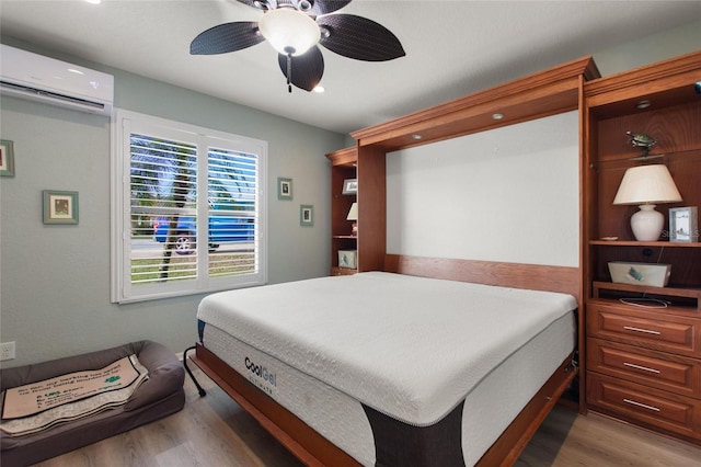 bedroom with a wall unit AC, ceiling fan, and hardwood / wood-style flooring