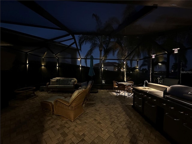 patio at night with glass enclosure, a grill, an outdoor hangout area, and sink