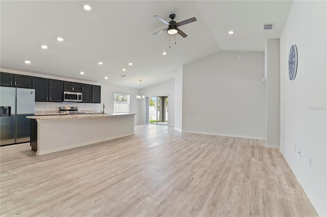 kitchen featuring light stone counters, hanging light fixtures, light hardwood / wood-style flooring, stainless steel appliances, and a kitchen island with sink