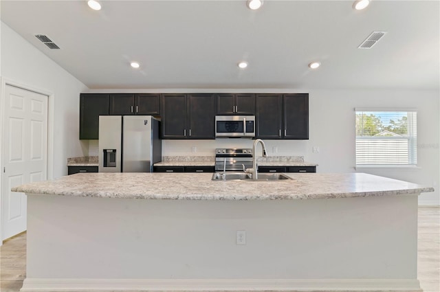 kitchen with sink, appliances with stainless steel finishes, light stone counters, a center island with sink, and light wood-type flooring