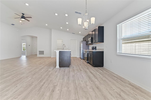 kitchen featuring ceiling fan with notable chandelier, an island with sink, pendant lighting, stainless steel appliances, and light hardwood / wood-style floors