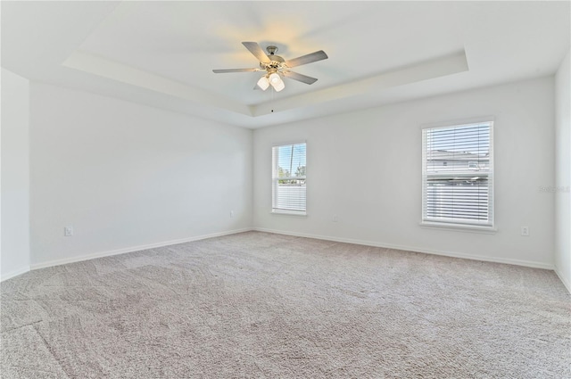 carpeted empty room with ceiling fan and a raised ceiling