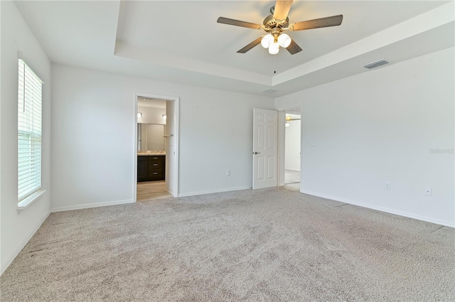 unfurnished bedroom featuring connected bathroom, light carpet, ceiling fan, and a tray ceiling