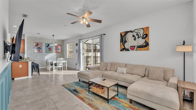 tiled living room featuring ceiling fan and brick wall