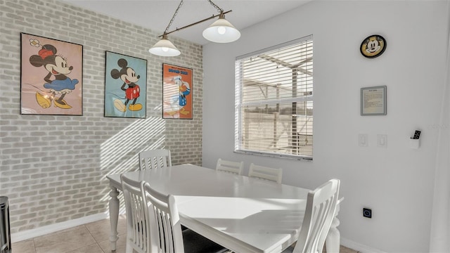 tiled dining area featuring baseboards and brick wall