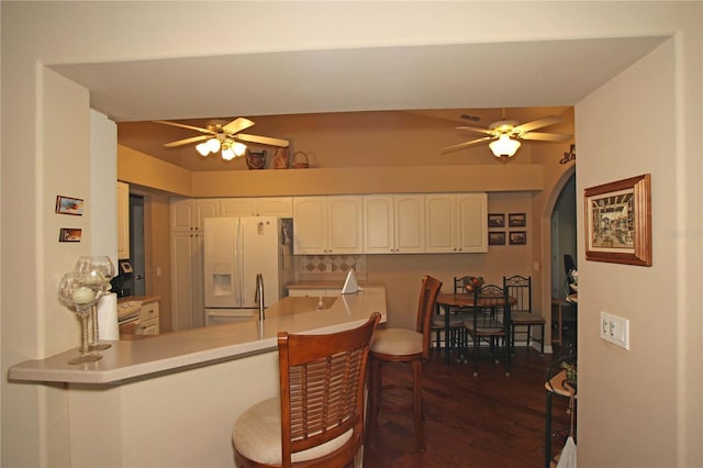 kitchen with white cabinets, ceiling fan, white fridge with ice dispenser, dark hardwood / wood-style flooring, and kitchen peninsula