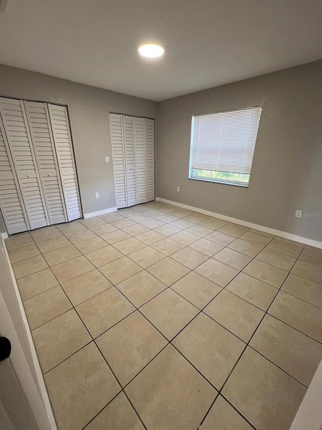 unfurnished bedroom featuring light tile patterned flooring and two closets