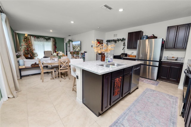 kitchen with sink, light stone counters, a kitchen island with sink, dark brown cabinets, and appliances with stainless steel finishes