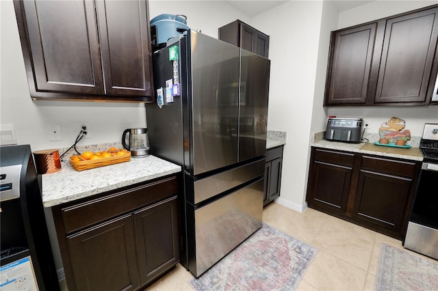 kitchen featuring light stone countertops, dark brown cabinetry, stainless steel range oven, fridge, and light tile patterned flooring