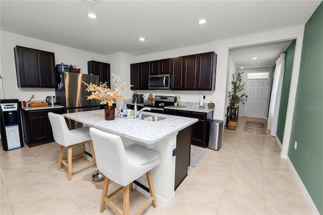 kitchen with dark brown cabinetry, sink, a kitchen bar, a center island with sink, and appliances with stainless steel finishes