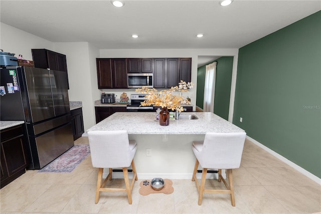 kitchen featuring a center island with sink, a kitchen breakfast bar, sink, dark brown cabinets, and stainless steel appliances