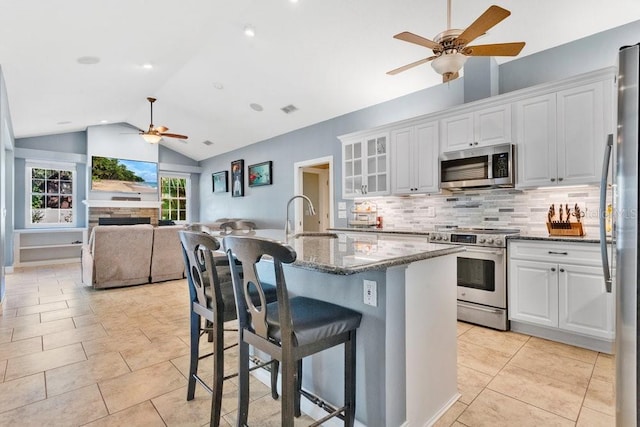 kitchen with white cabinetry, sink, stainless steel appliances, dark stone counters, and lofted ceiling