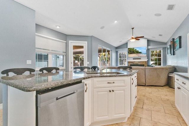 kitchen with lofted ceiling, a kitchen island with sink, sink, stainless steel dishwasher, and white cabinetry