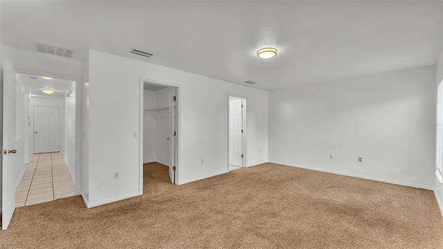 unfurnished bedroom featuring a walk in closet, light colored carpet, and a closet