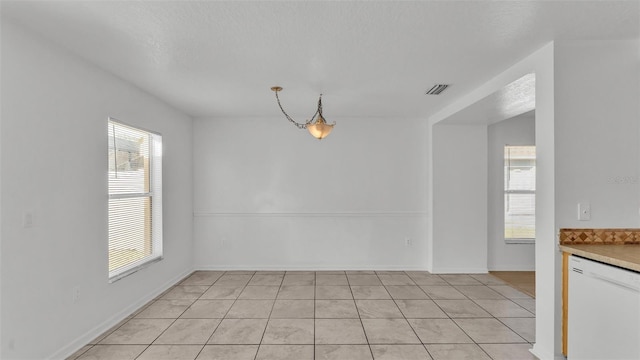 unfurnished dining area with light tile patterned flooring, a healthy amount of sunlight, and a textured ceiling