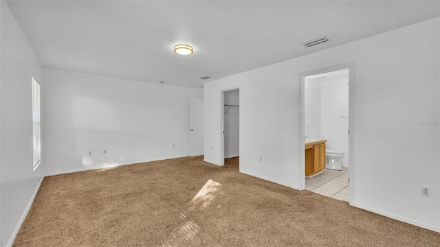 unfurnished bedroom with a spacious closet, light colored carpet, ensuite bath, and a closet