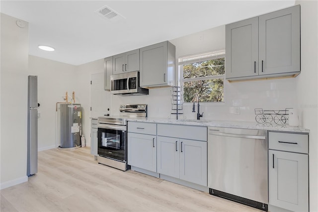 kitchen featuring light stone counters, stainless steel appliances, sink, water heater, and light hardwood / wood-style floors