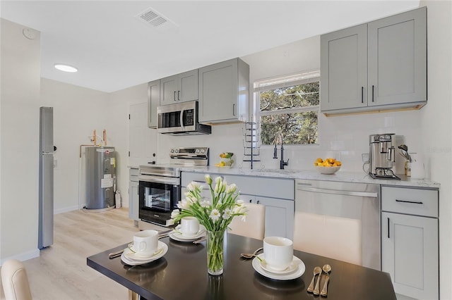 kitchen with sink, water heater, light stone counters, appliances with stainless steel finishes, and light wood-type flooring