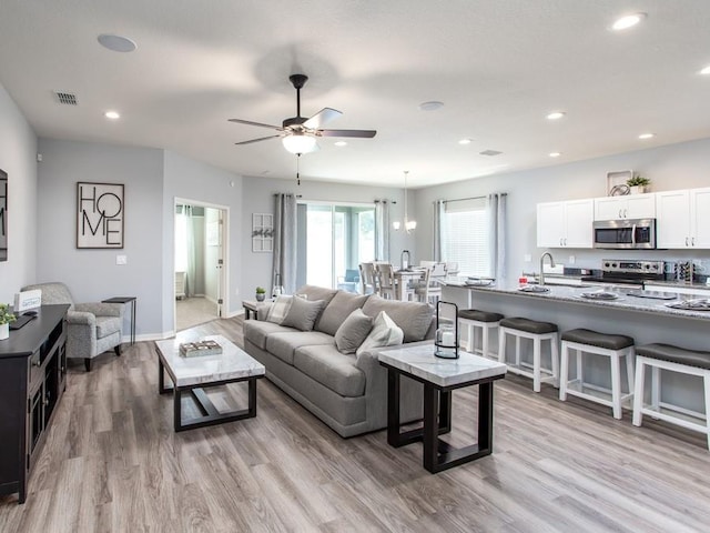 living room with light hardwood / wood-style flooring, ceiling fan with notable chandelier, and sink