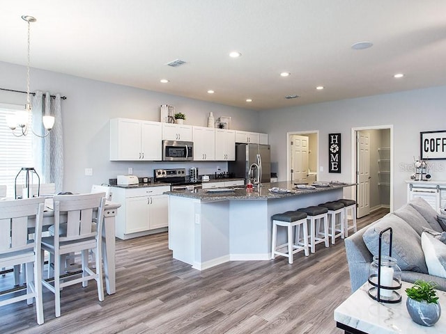 kitchen featuring pendant lighting, a kitchen island with sink, white cabinets, light hardwood / wood-style flooring, and appliances with stainless steel finishes