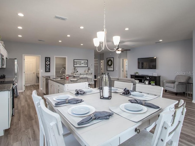 dining area with sink, ceiling fan with notable chandelier, and hardwood / wood-style flooring