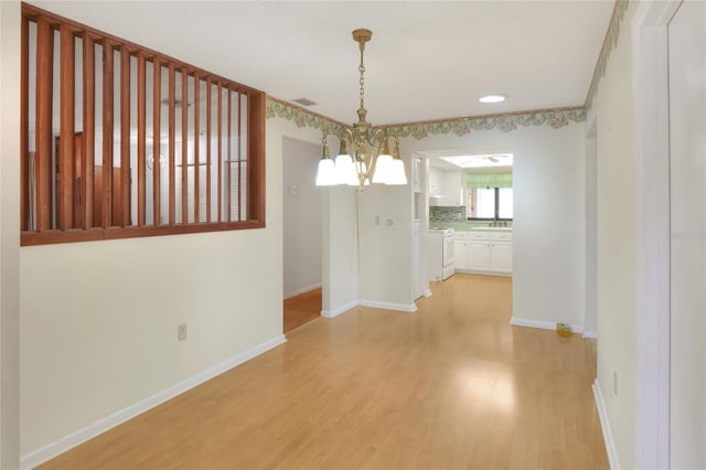 unfurnished dining area with sink, a chandelier, and light wood-type flooring