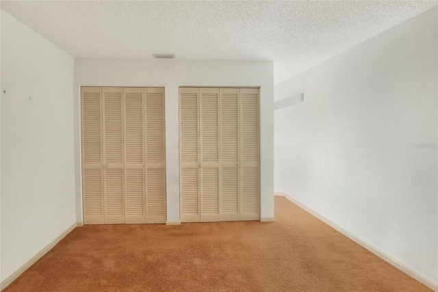 unfurnished bedroom with a textured ceiling, carpet floors, and two closets