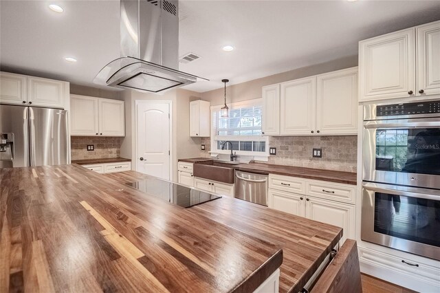 kitchen with butcher block counters, white cabinetry, sink, stainless steel appliances, and island exhaust hood