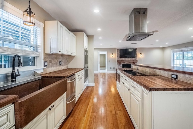 kitchen featuring white cabinetry, stainless steel appliances, hanging light fixtures, extractor fan, and light wood-type flooring