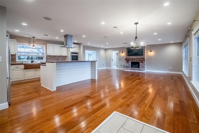 kitchen with white cabinetry, stainless steel oven, wall chimney range hood, and light wood-type flooring