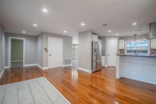 kitchen featuring white cabinetry, light hardwood / wood-style flooring, backsplash, stainless steel fridge, and pendant lighting