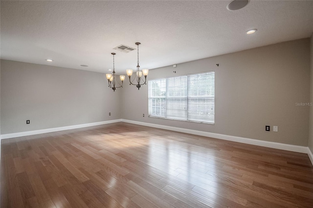 unfurnished room featuring a chandelier, wood-type flooring, and a textured ceiling