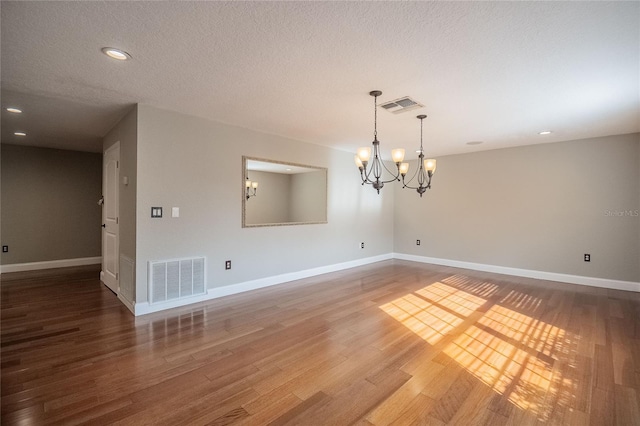 empty room with a textured ceiling, a notable chandelier, and hardwood / wood-style flooring