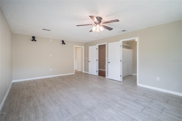 unfurnished bedroom featuring ceiling fan, light wood-type flooring, a walk in closet, and a closet