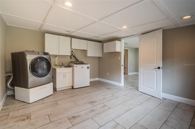 clothes washing area with cabinets, light hardwood / wood-style floors, washer / clothes dryer, and sink